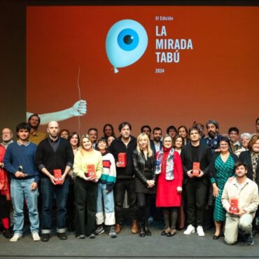 Grupo de personas en una entrega de premios del festival La mirada tabú posando en el photocall con el póster del festival detrás.
