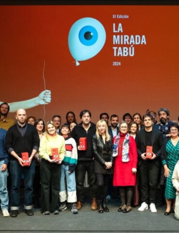 Grupo de personas en una entrega de premios del festival La mirada tabú posando en el photocall con el póster del festival detrás.