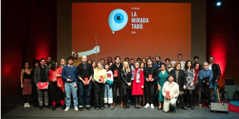 Grupo de personas en una entrega de premios del festival La mirada tabú posando en el photocall con el póster del festival detrás.